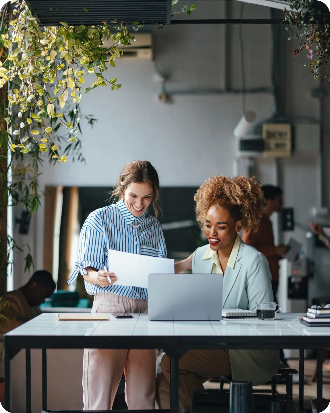 Two coworkers in a professional setting looking at a paper and a laptop and discussing Duo's 2FA locking down security by verifying users through two authentication factors.