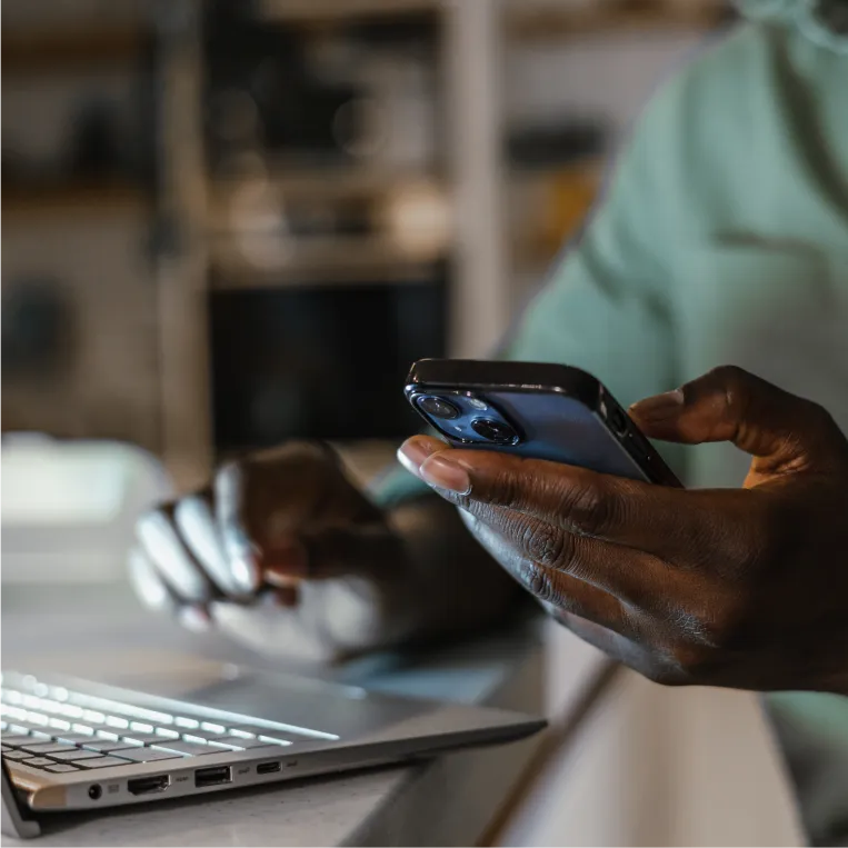 Person using phone and laptop indoors.
