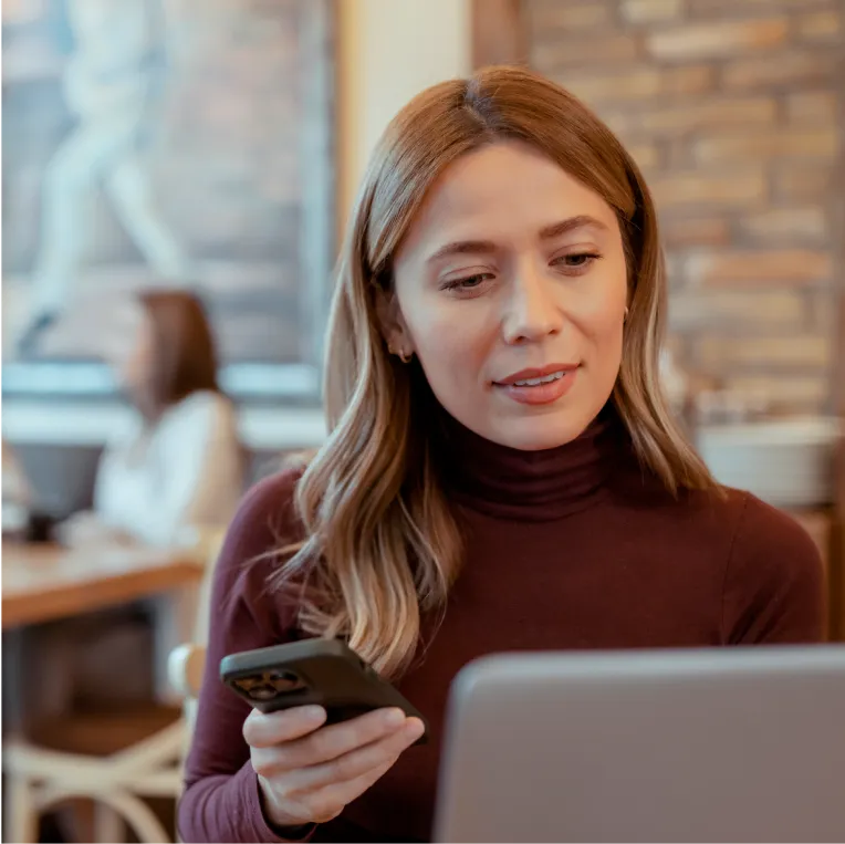 Person in maroon sweater using phone and laptop.