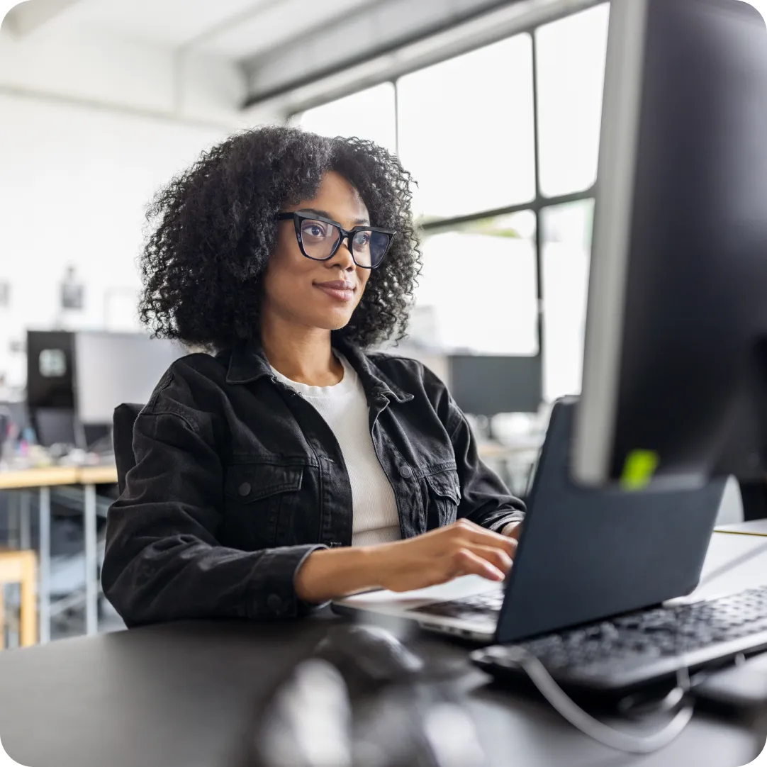 Professional at their desk with glasses on, engaging with Duo support on their laptop screen while looking at their desktop monitor.