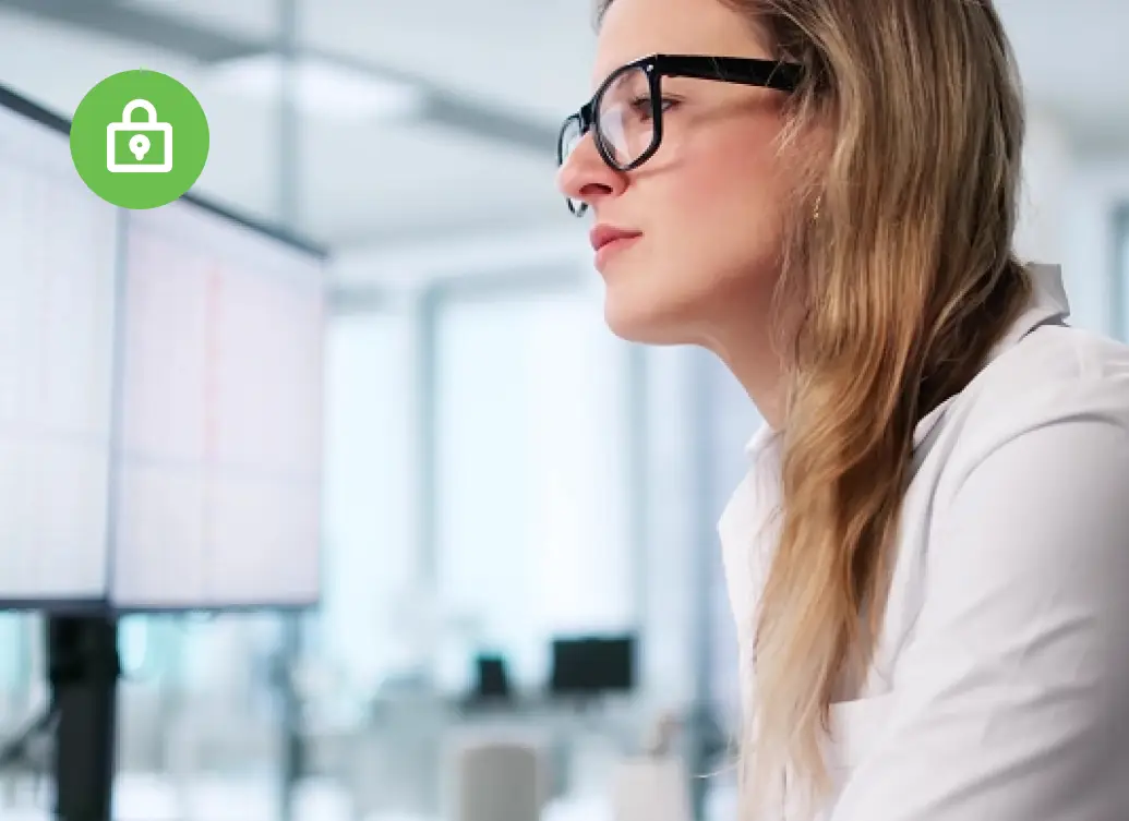 A woman wearing glasses looks at computer monitors in a bright, modern office