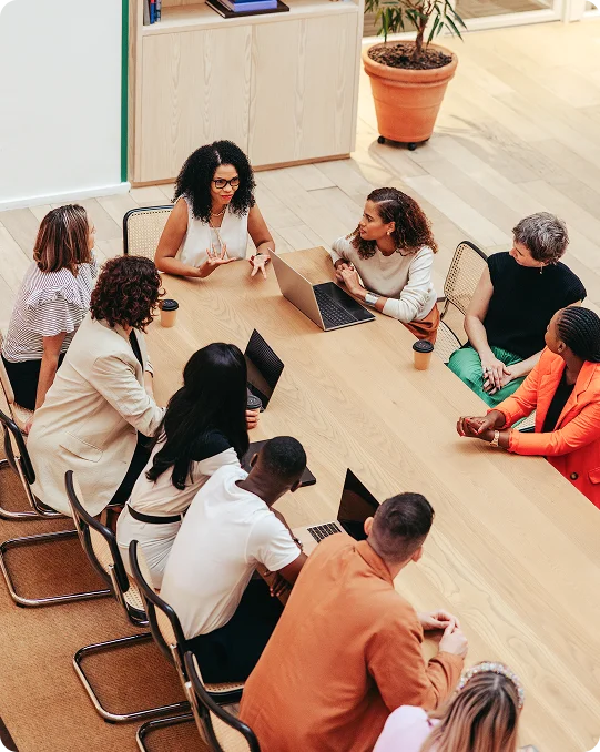 Professionals gathered around a conference table discussing ideas, with laptops and coffee cups visible in a modern office