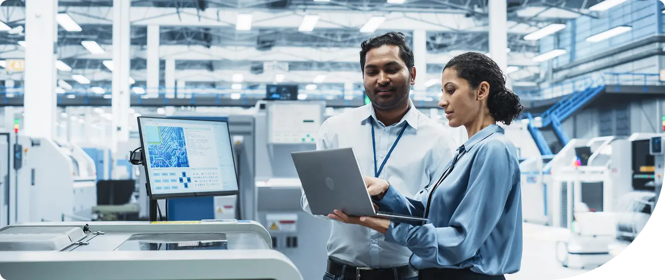 Two IT professionals review customer identity and access management configurations on a laptop in a modern manufacturing facility