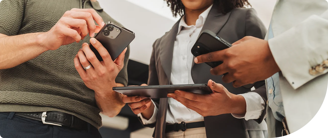 Three professionals reviewing access authentication across mobile devices and a tablet, representing multi-device identity verification