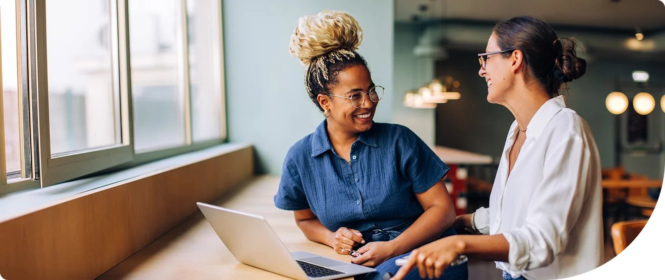Two women colleagues conversing and discussing business over a laptop