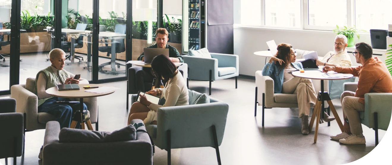 Groups of coworkers collaborate in a bright, open office lounge with laptops and notebooks