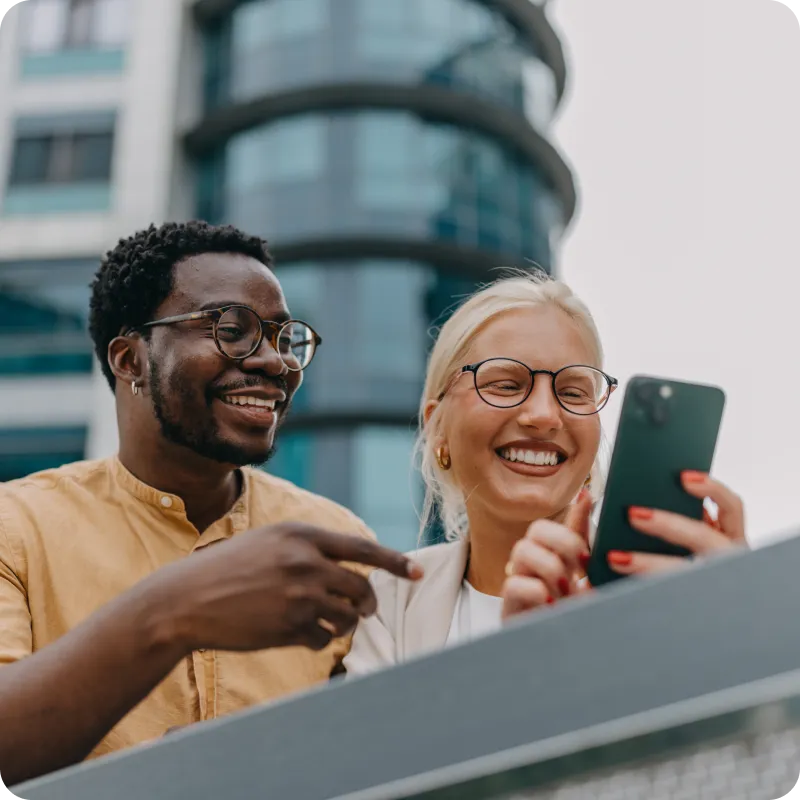 Two colleagues smiling while looking at a phone and discussing why investing in FSP cybersecurity is important