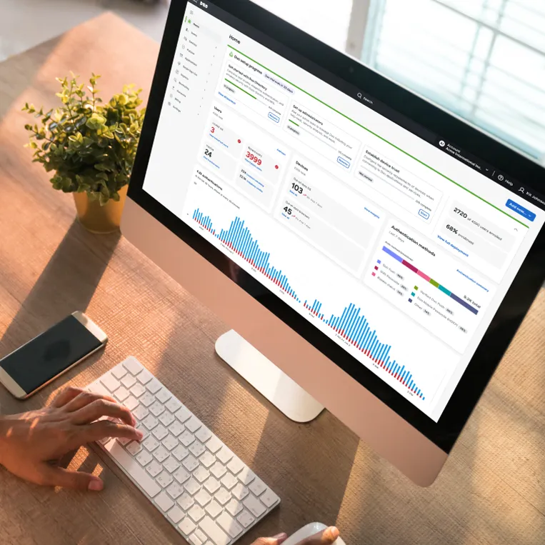 High angle photo of a monitor sitting on a desk. On the screen is the Duo admin dashboard with bar charts and statistics.