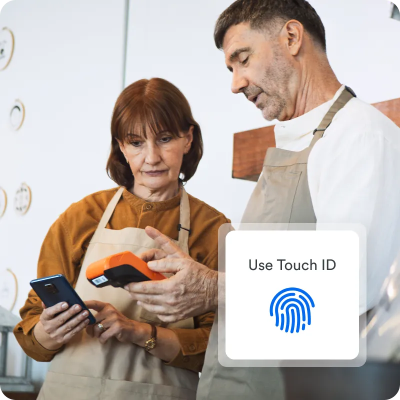 Retail employee holds card reader with Use Touch ID icon, demonstrating transaction to coworker