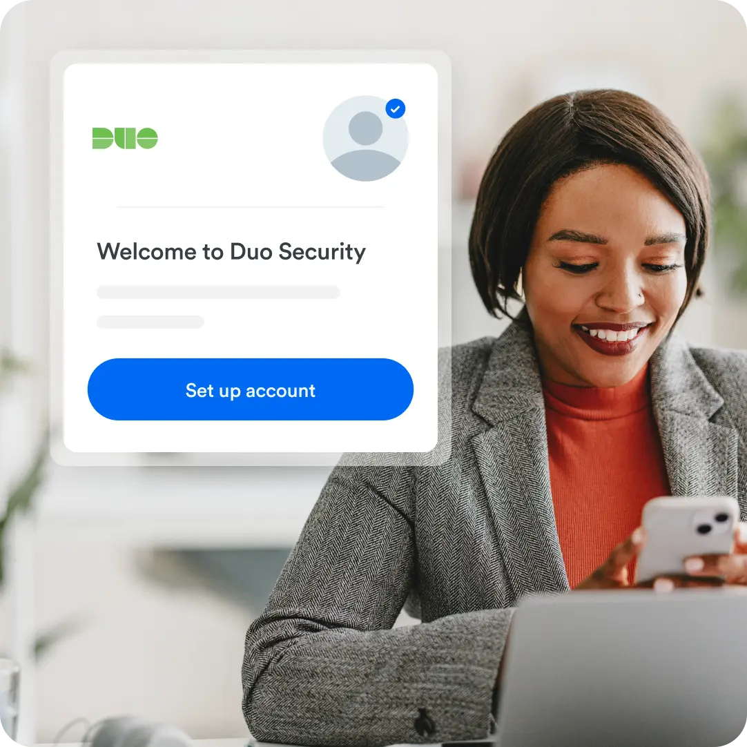 Professional sitting at their desk with laptop and looking down at their phone that shows a welcome to Duo Security log in to set up their account in a screenshot in the foreground.