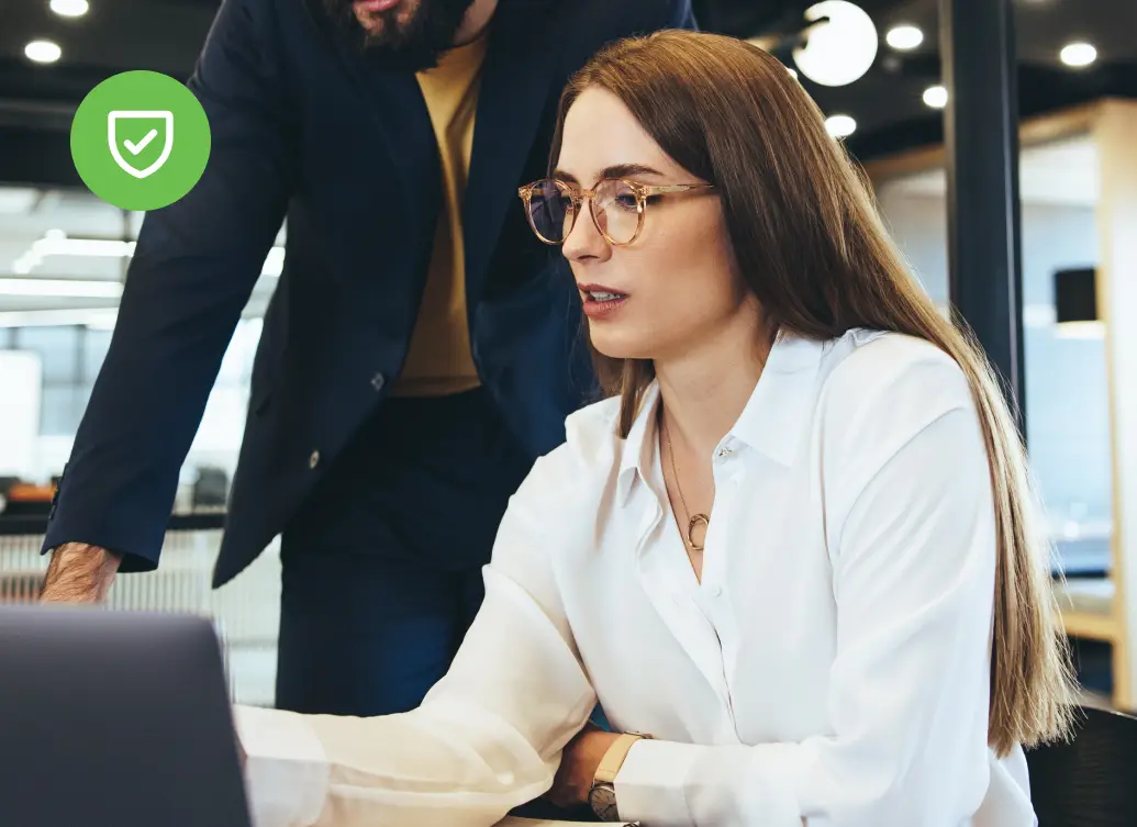 Two IT professionals collaborating at a laptop while a colleague works in the background