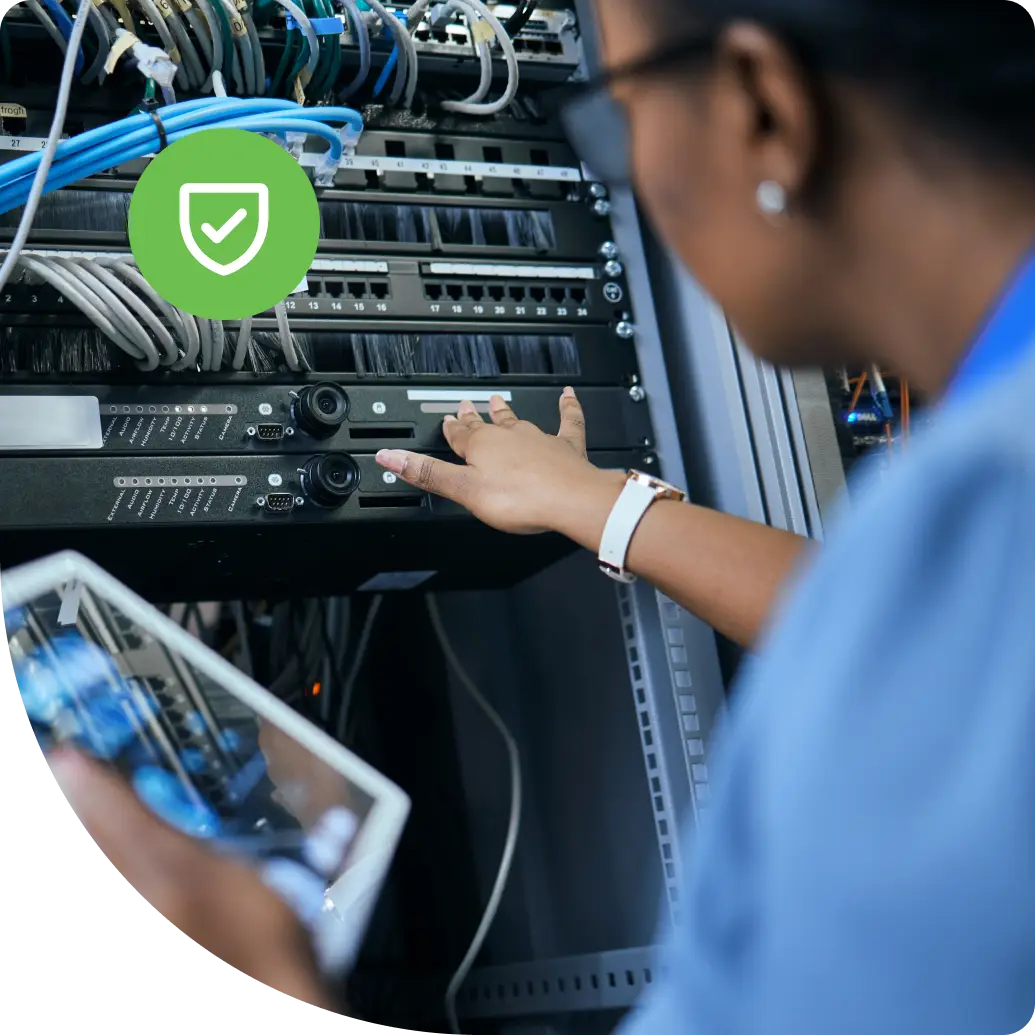 A network technician configuring rack-mounted network switches while referencing a tablet.