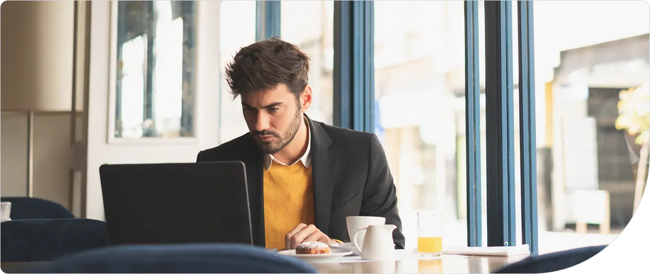 A business professional works intently on a laptop at a caf&eacute; table, illustrating the need for least privilege access controls for remote workers