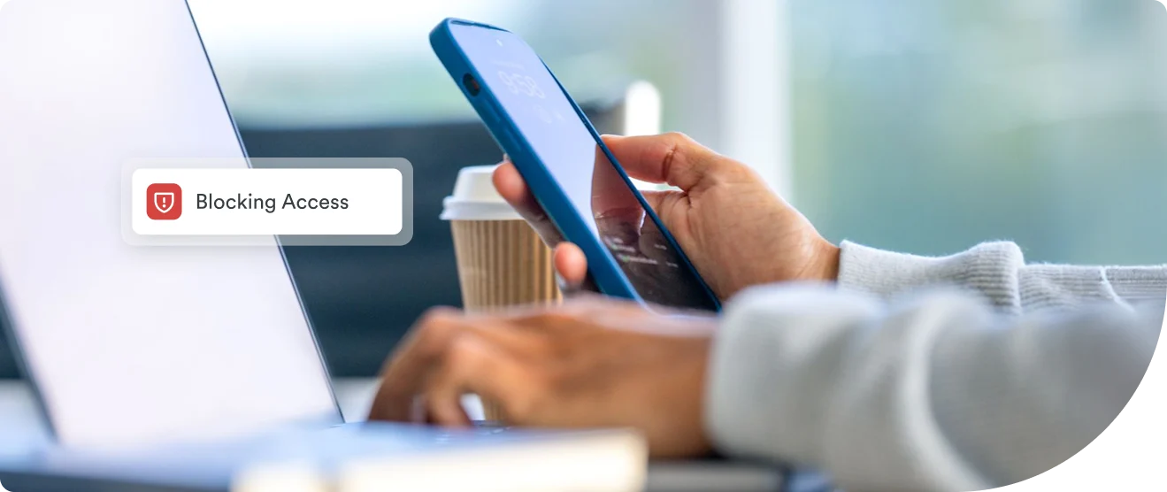 A close-up of a hand holding a smartphone displaying a Blocking Access alert, showing how Duo Security stops unauthorized phishing-related login attempts